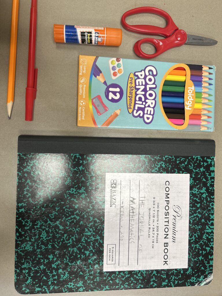 Cuaderno, lápices, bolígrafo, tijeras y pegamento sobre una mesa.